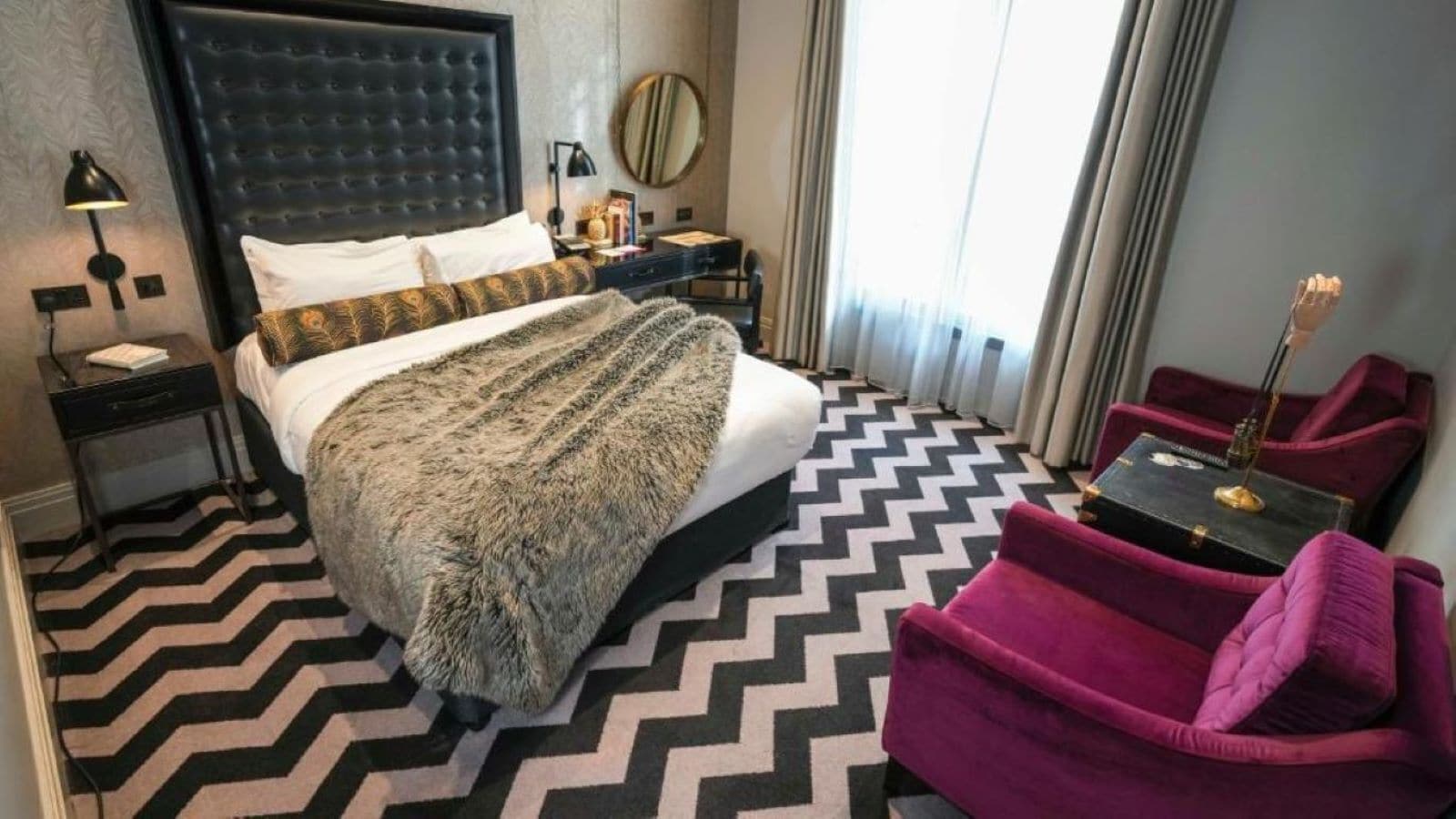 Una habitación de hotel con una cama grande, una mesita de noche, un escritorio, una silla y una ventana con cortinas.