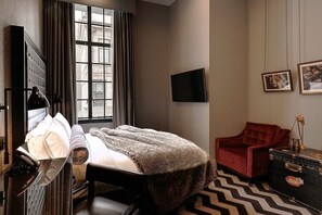 A hotel room with a bed, a red armchair, a television, and a large window.
