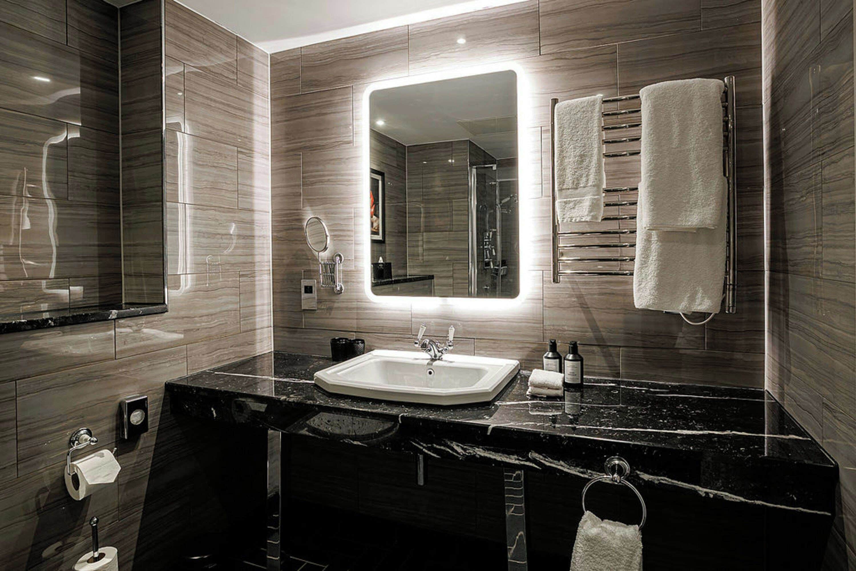 A modern bathroom with a large mirror, a sink, and a towel rack.