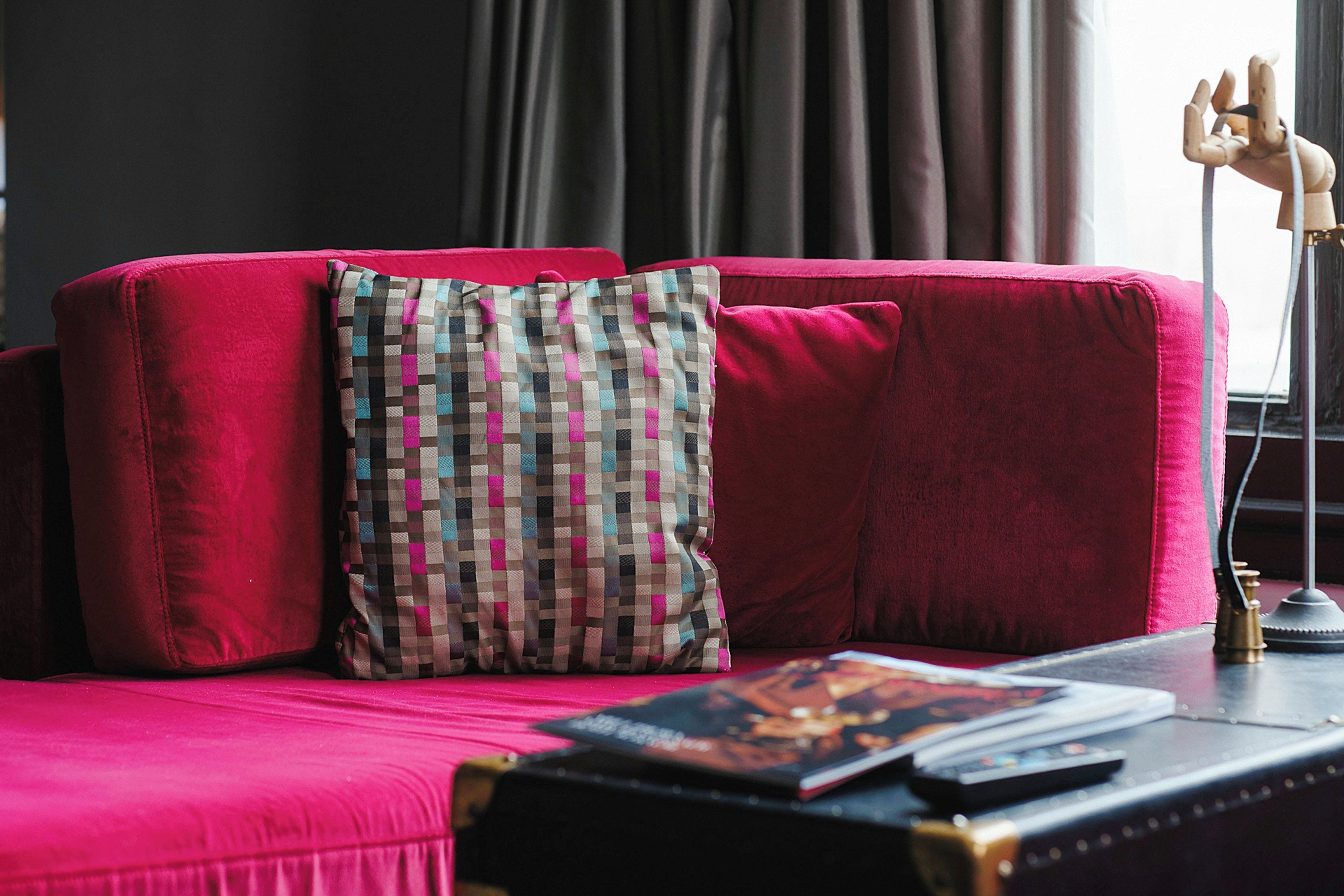 A red sofa with a checkered pillow and a book on a side table.