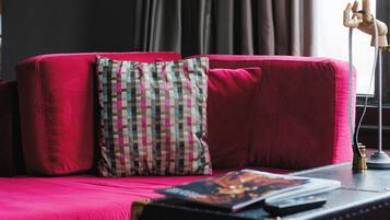 A red sofa with a checkered pillow and a book on a side table.