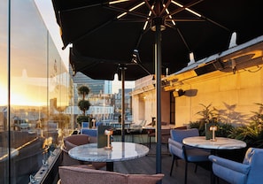 An outdoor seating area with round tables and chairs, a glass wall with a city view, and a modern light fixture.