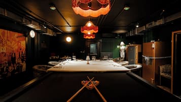 A dimly lit room with a pool table, billiard cues, and a billiard ball.