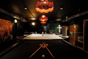 Una habitación tenuemente iluminada con una mesa de billar, tacos y una bola de billar.