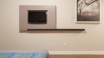 A bedroom with a bed, a mounted TV, and a framed picture on the wall.