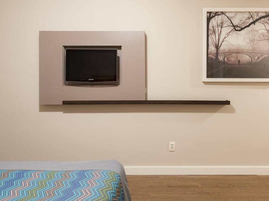 A bedroom with a bed, a mounted TV, and a framed picture on the wall.