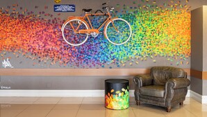 Una habitación con un cuadro abstracto de colores en la pared, una bicicleta colgada en la pared, un sillón de cuero y un cubo de basura.