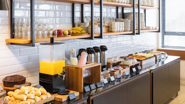 Un buffet con diferentes opciones de comida, incluyendo pasteles, frutas y bebidas, dispuestas en estantes y mostradores de madera.