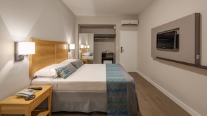 Habitación de hotel con cama, mesita de noche con teléfono, televisor montado en la pared y unidad de aire acondicionado.