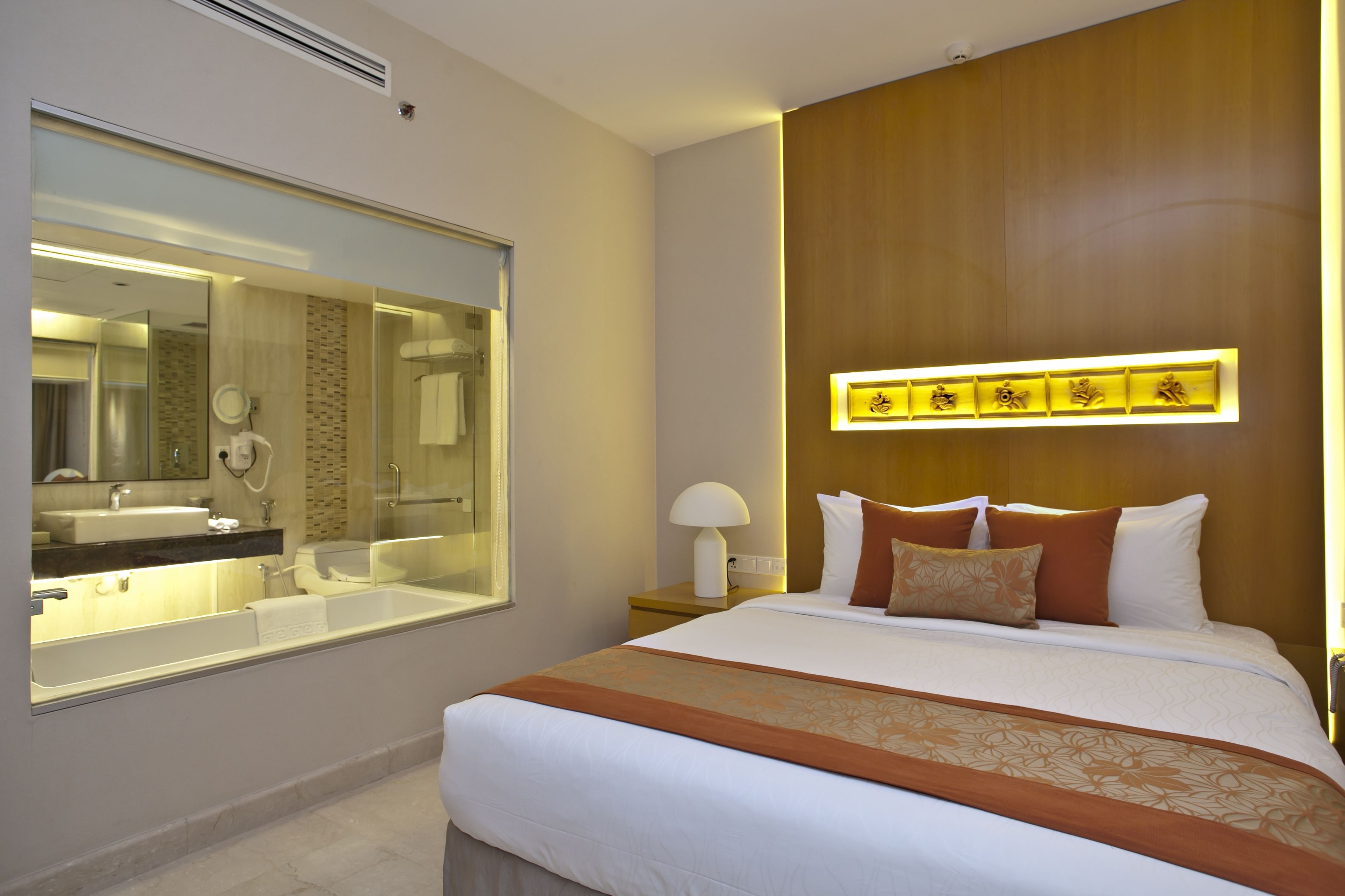 Une chambre d’hôtel avec un grand lit, une salle de bain dotée d’une douche à parois de verre et un luminaire fixé au mur.
