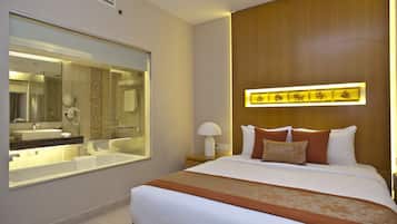 Une chambre d’hôtel avec un grand lit, une salle de bain dotée d’une douche à parois de verre et un luminaire fixé au mur.