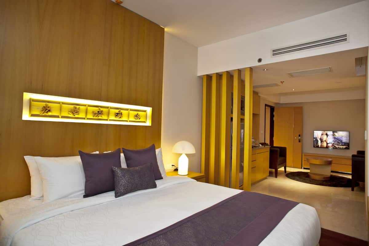 A hotel room with a large bed, a TV, a desk, and a wooden accent wall.