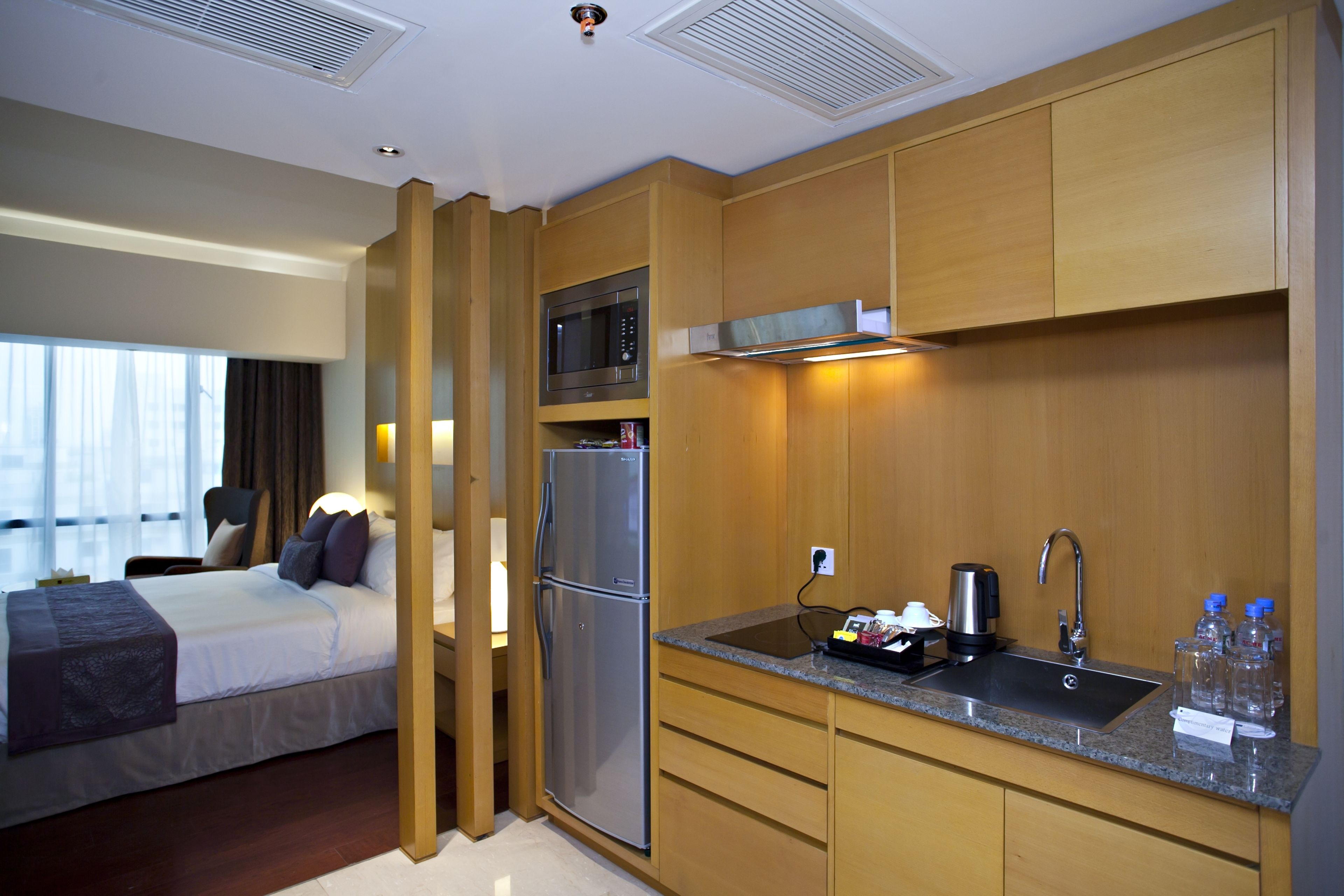 A hotel room with a bed, a kitchenette with a microwave, refrigerator, sink, and cabinets.