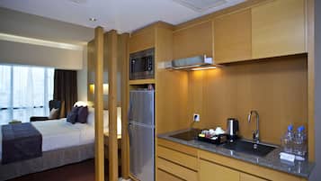 A hotel room with a bed, a kitchenette with a microwave, refrigerator, sink, and cabinets.