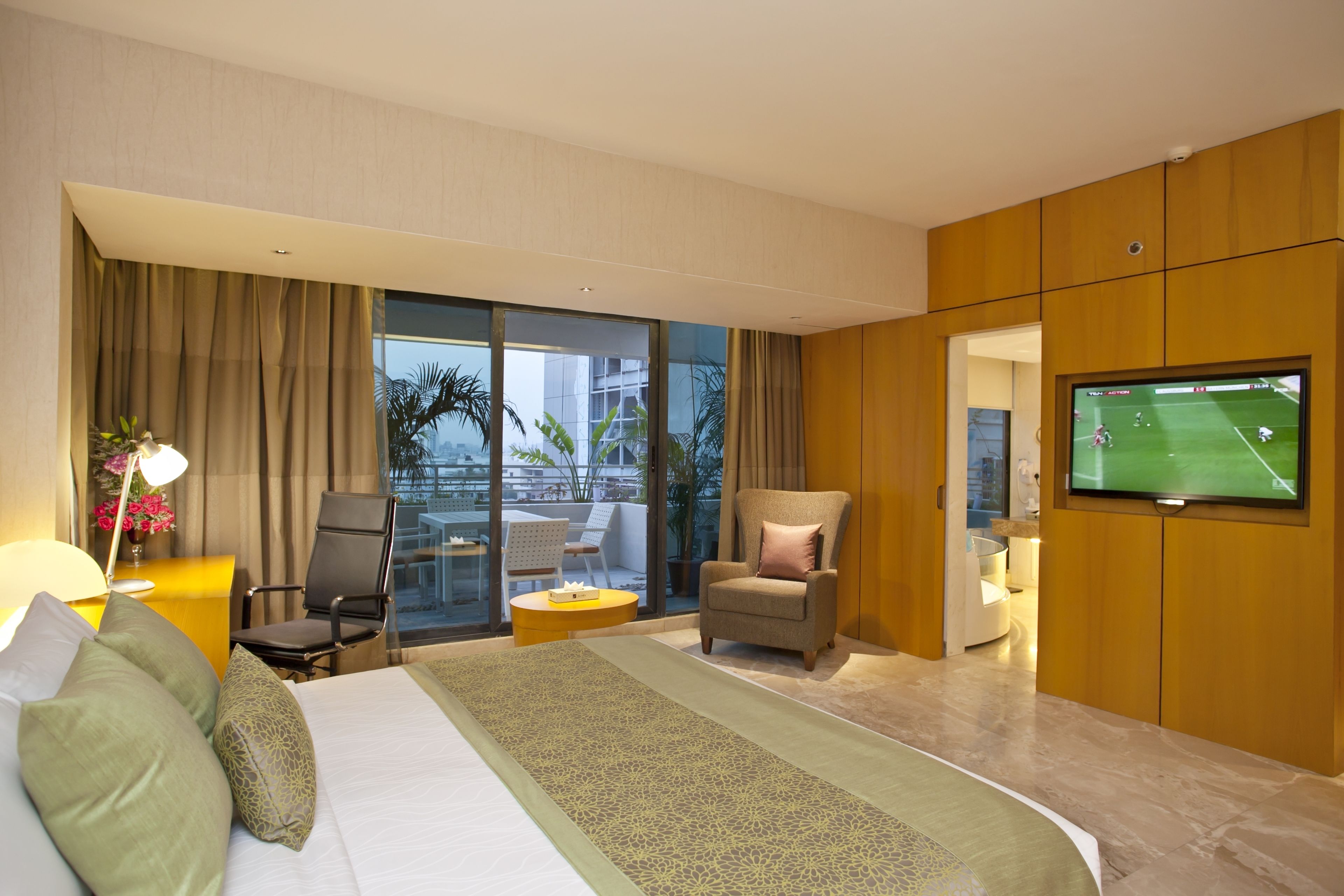 A hotel room with a large bed, a TV, a chair, a desk, and a view of the city.