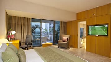 A hotel room with a large bed, a TV, a chair, a desk, and a view of the city.