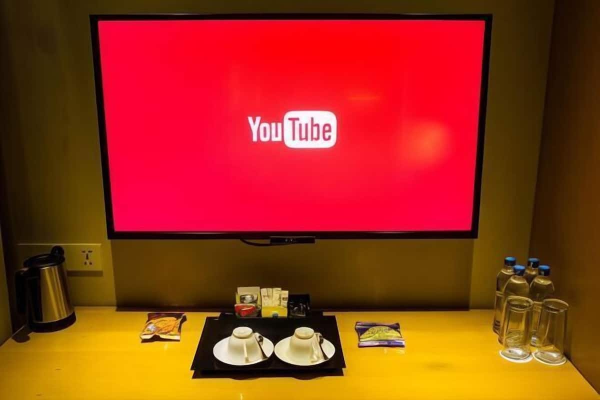 A hotel room with a flat-screen TV displaying the YouTube logo, a coffee maker, a tray with cups and snacks, and bottled water.