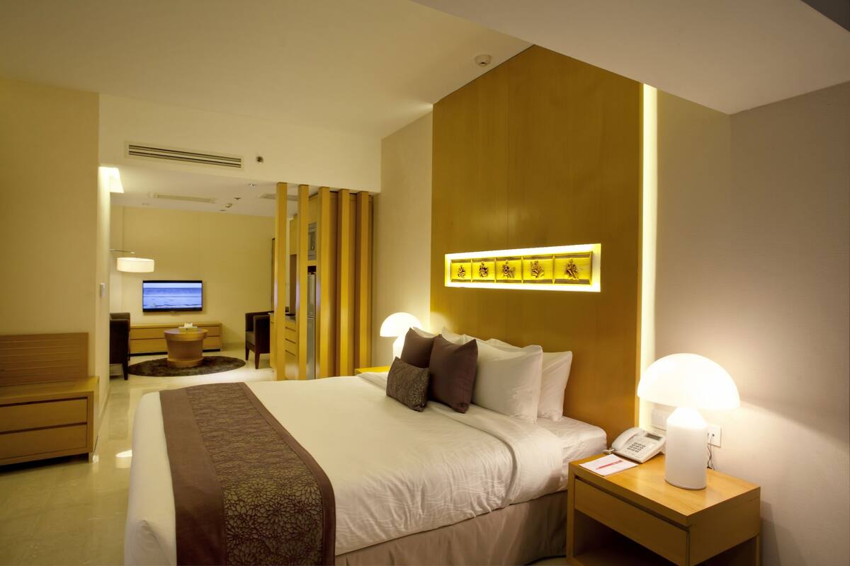 A hotel room with a large bed, bedside lamps, a flat-screen TV, a wooden panel wall, and a small table with a lamp.