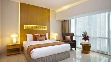 A modern hotel room with a large bed, bedside lamps, a chair, a side table, and a large window with curtains.