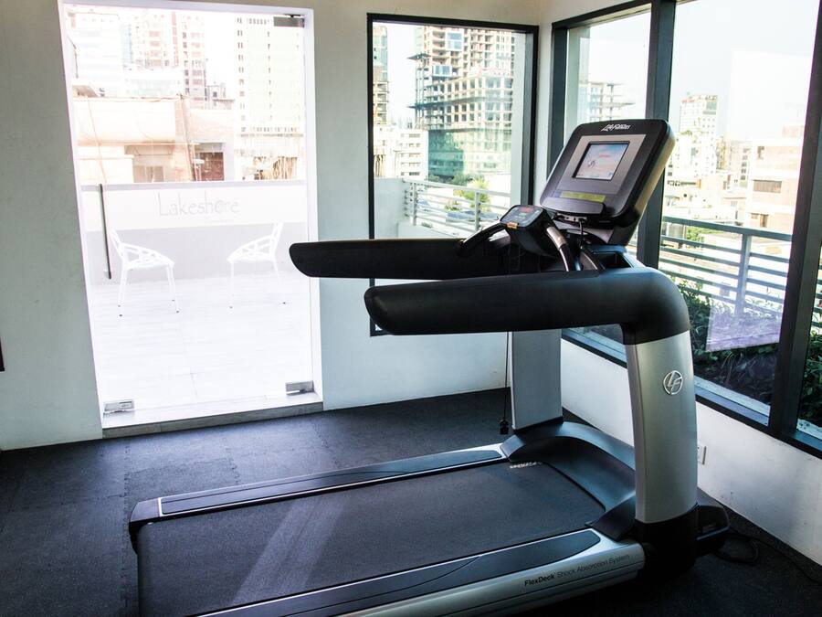 A treadmill in a room with large windows, a scale, and a chair.