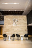 Un área de recepción con pared de piedra, cuatro sillas negras y una mesa blanca.