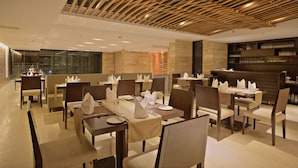 A modern restaurant with neatly arranged tables and chairs, a wooden ceiling design, and a bar area with glassware. - Lakeshore Banani (Dhaka)