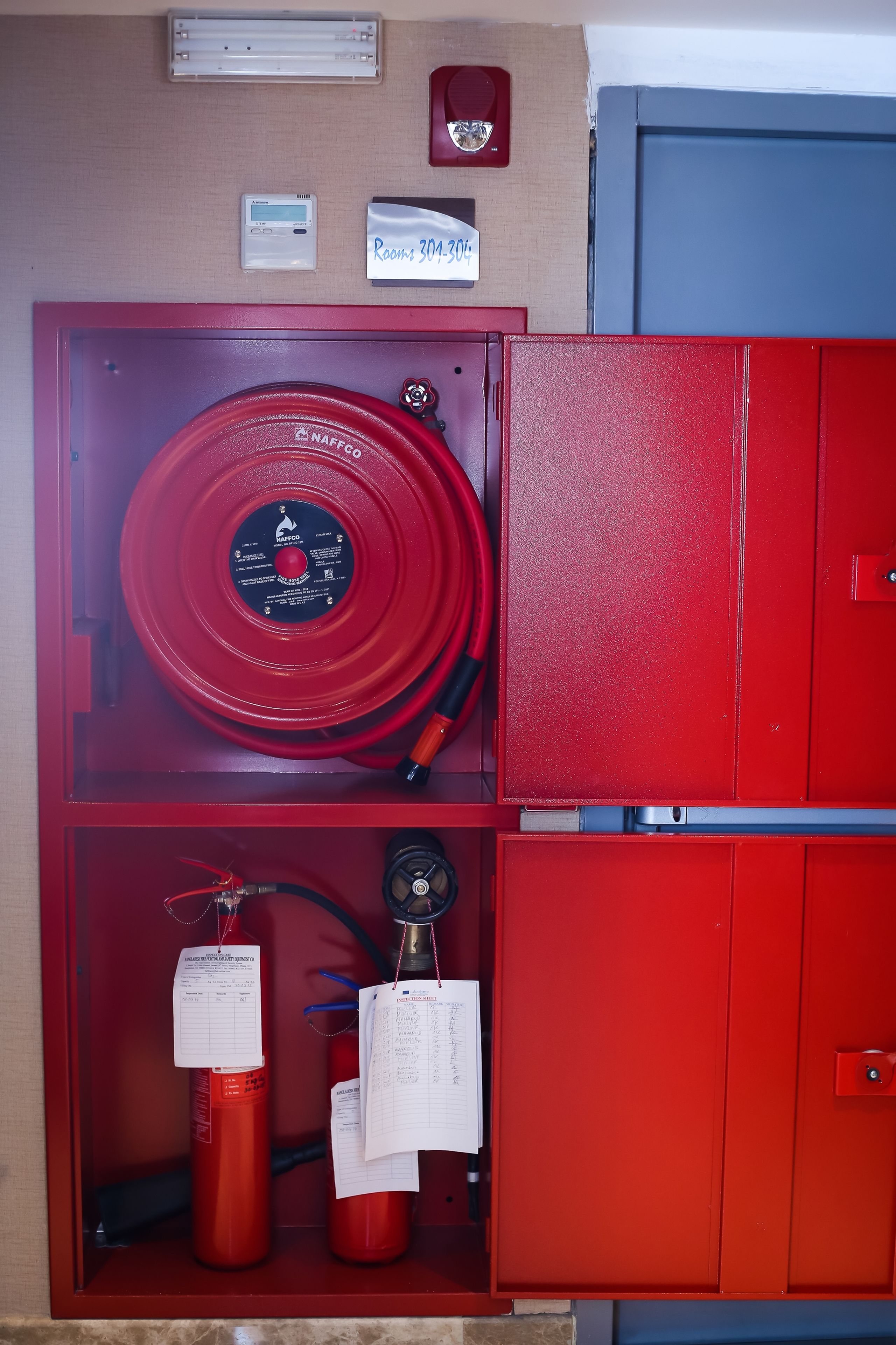 Ein roter Schrank für Feuerlöscher mit einem Feuerwehrschlauch und zwei Feuerlöschern.