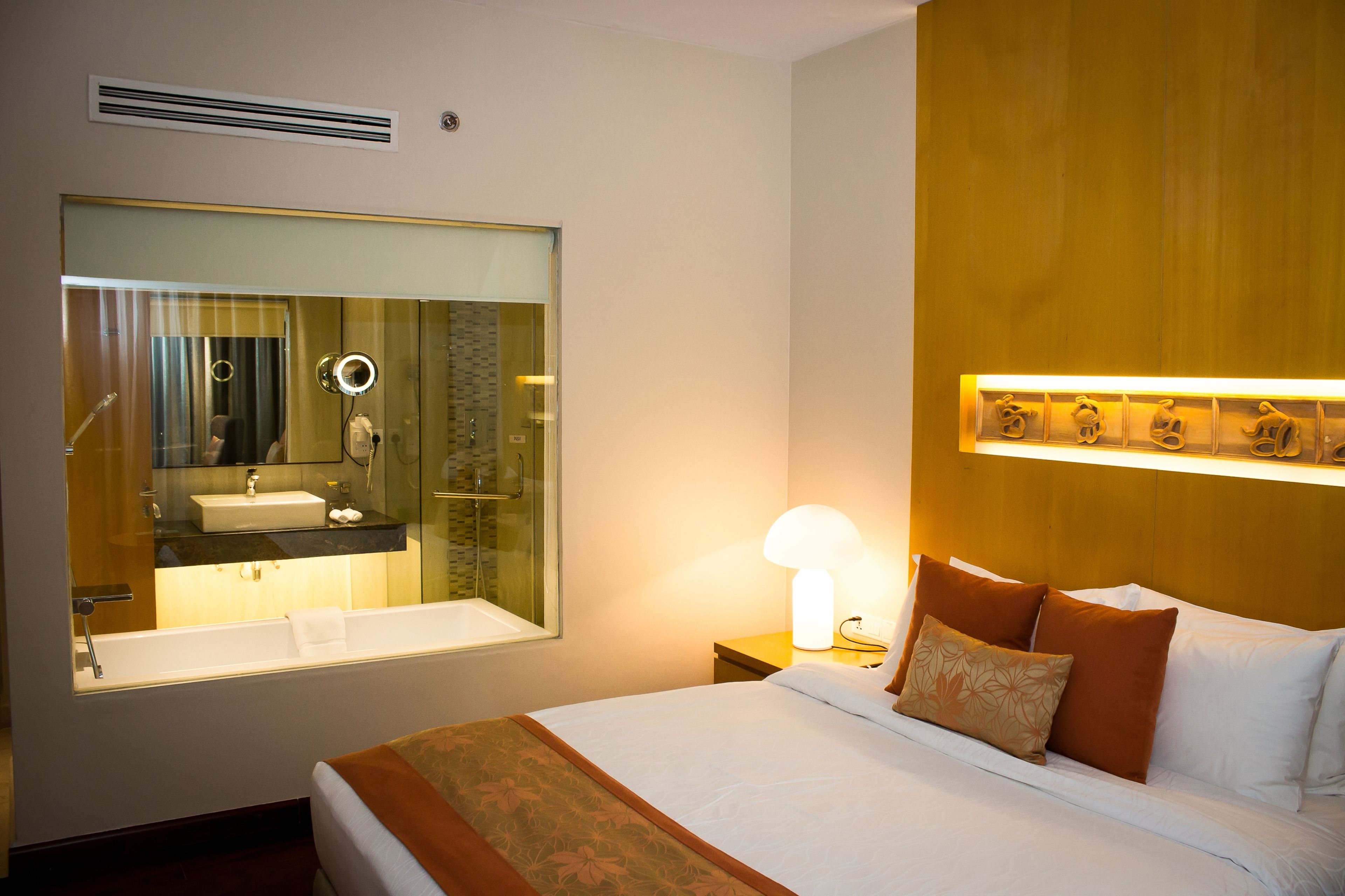 Habitación de hotel con una cama grande, un baño con espejo y una lámpara de pared.