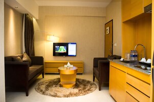 Una habitación de hotel moderna con sofá, una pequeña mesa redonda, televisor, zona de cocina y baño.