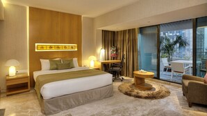 A modern hotel room with a large bed, a desk, a chair, a small table, and a view of the outdoors. - Lakeshore Banani (Dhaka)