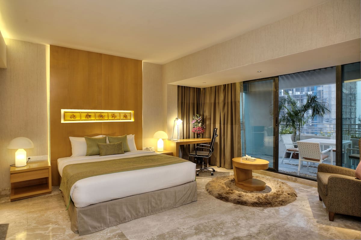 A modern hotel room with a large bed, a desk, a chair, a small table, and a view of the outdoors.