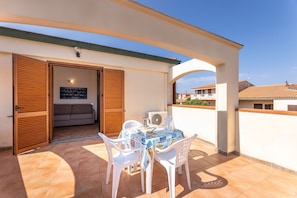An outdoor patio with a table and chairs, a sofa inside, and a view of neighboring buildings.