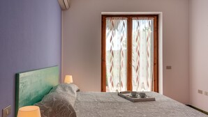 Een slaapkamer met een bed, een nachtkastje met een lamp, een raam met gordijnen en een dienblad met een kopje en schotel op het bed.