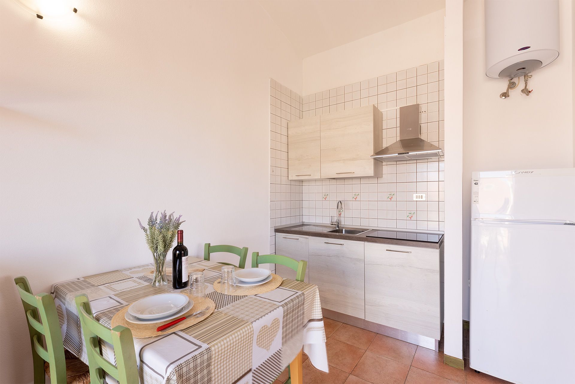 A compact kitchen with white tiles, a built-in stove, and a white refrigerator.