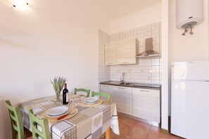A compact kitchen with white tiles, a built-in stove, and a white refrigerator. - Residence Le Pavoncelle (Santa Teresa di Gallura)