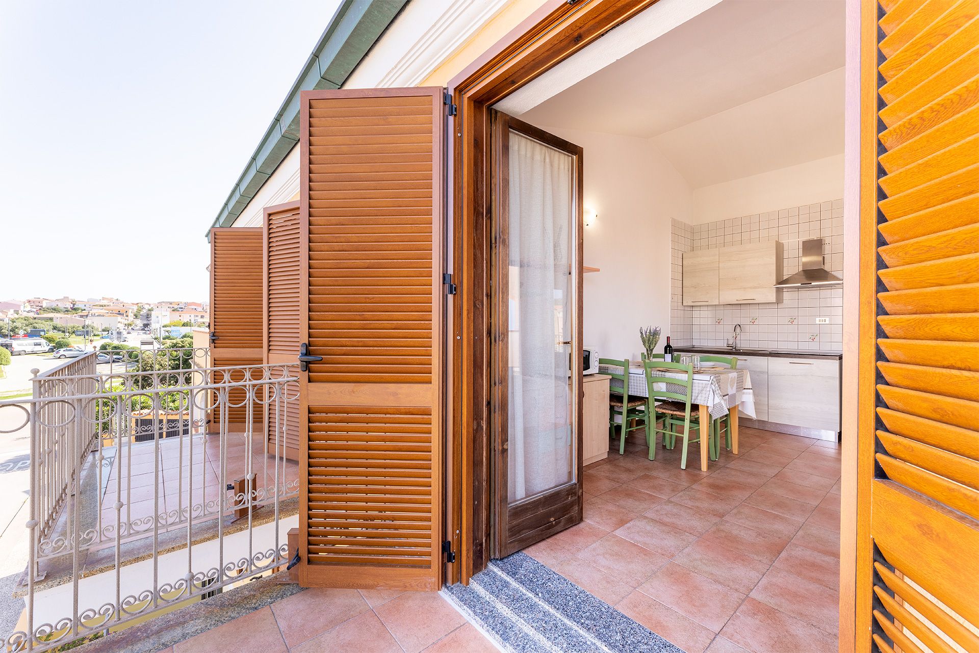Un balcón con una puerta de madera, un área de comedor con mesa y sillas, y una cocina con paredes de cerámica.