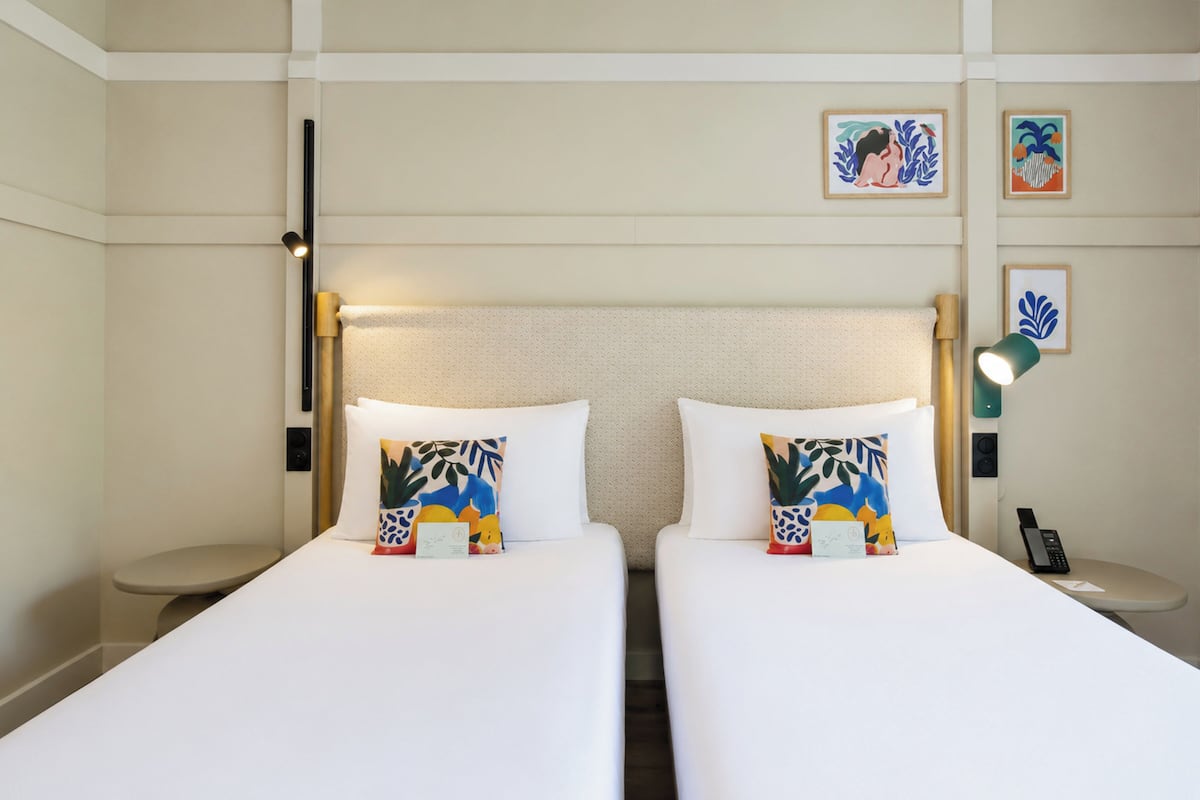 Habitación de hotel con dos camas, una mesita de noche con lámpara, teléfono y una obra de arte en la pared.