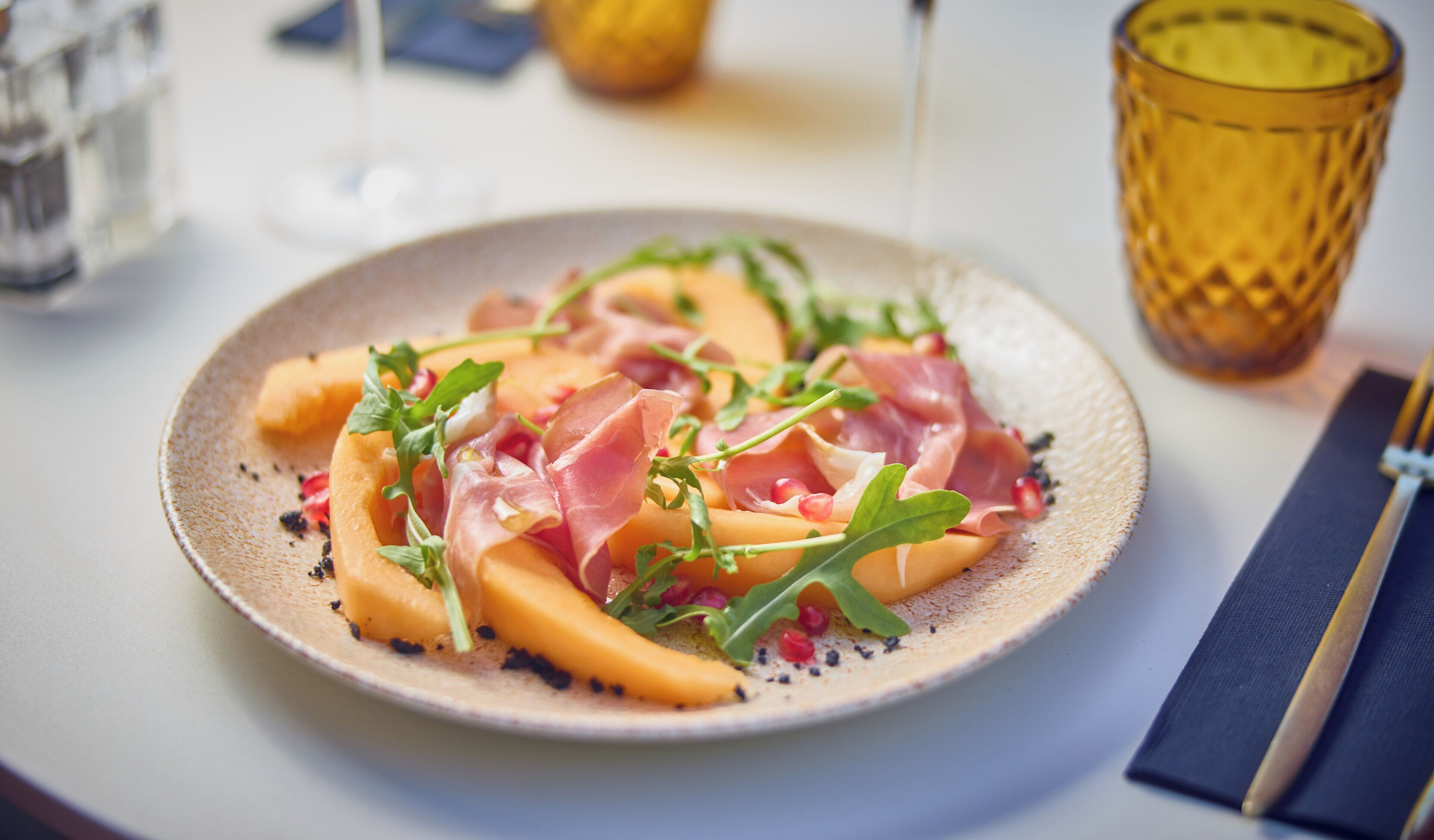 A plate of food with prosciutto and arugula on a textured plate.