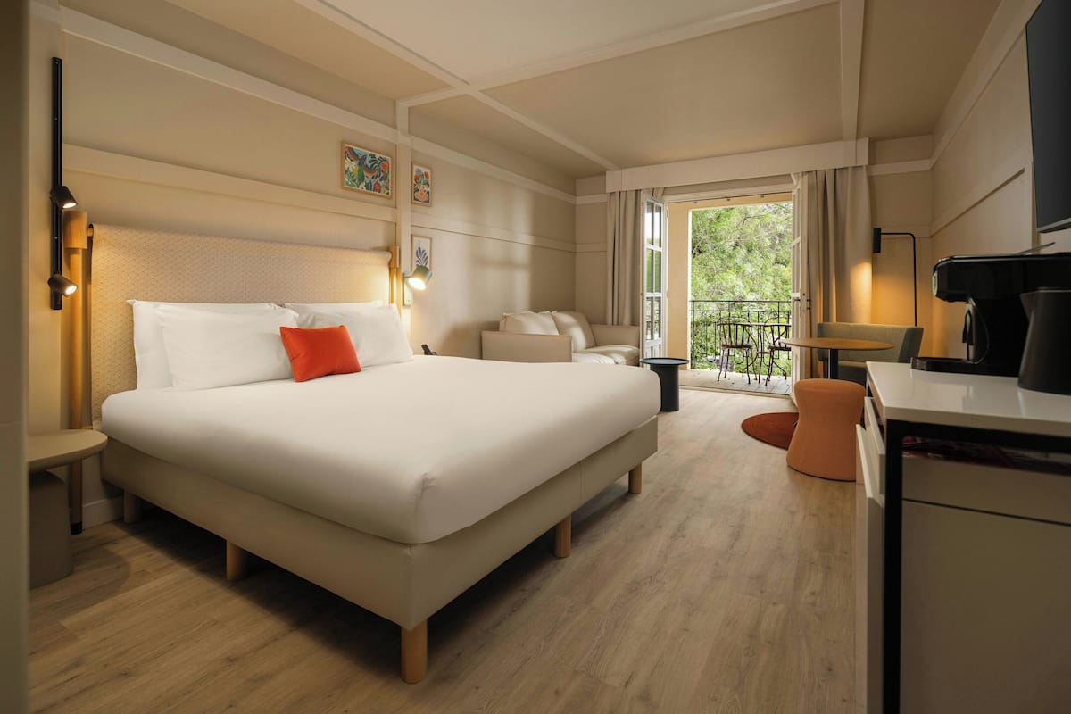 Habitación de hotel con una cama grande, un escritorio, una silla y un balcón con mobiliario exterior.