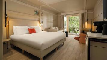 A hotel room with a large bed, a desk, a chair, and a balcony with outdoor furniture.