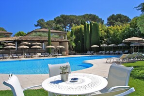 A poolside area with lounge chairs, umbrellas, and a table with a potted plant.
