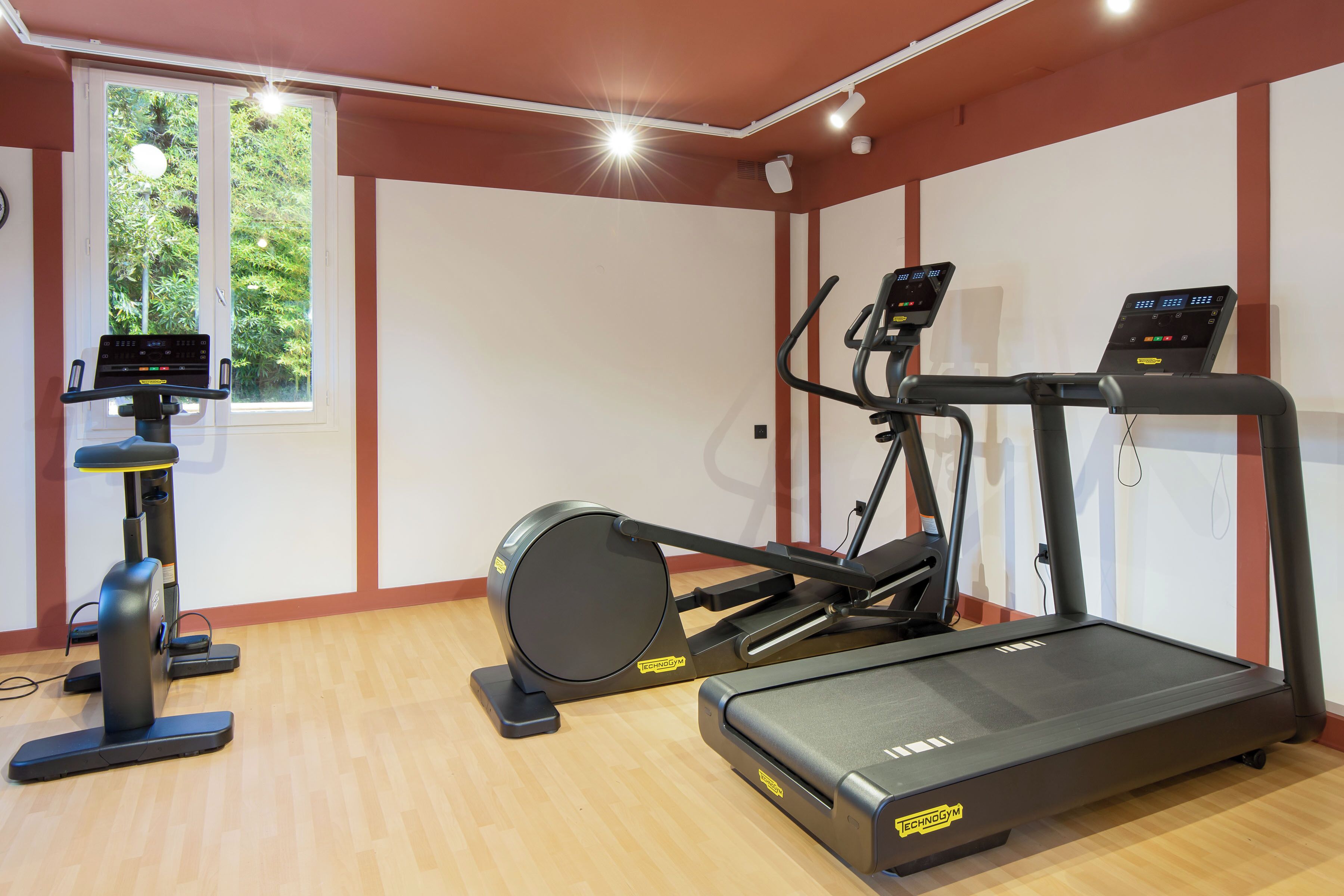 A gym with cardio equipment, a window, and a wooden floor.