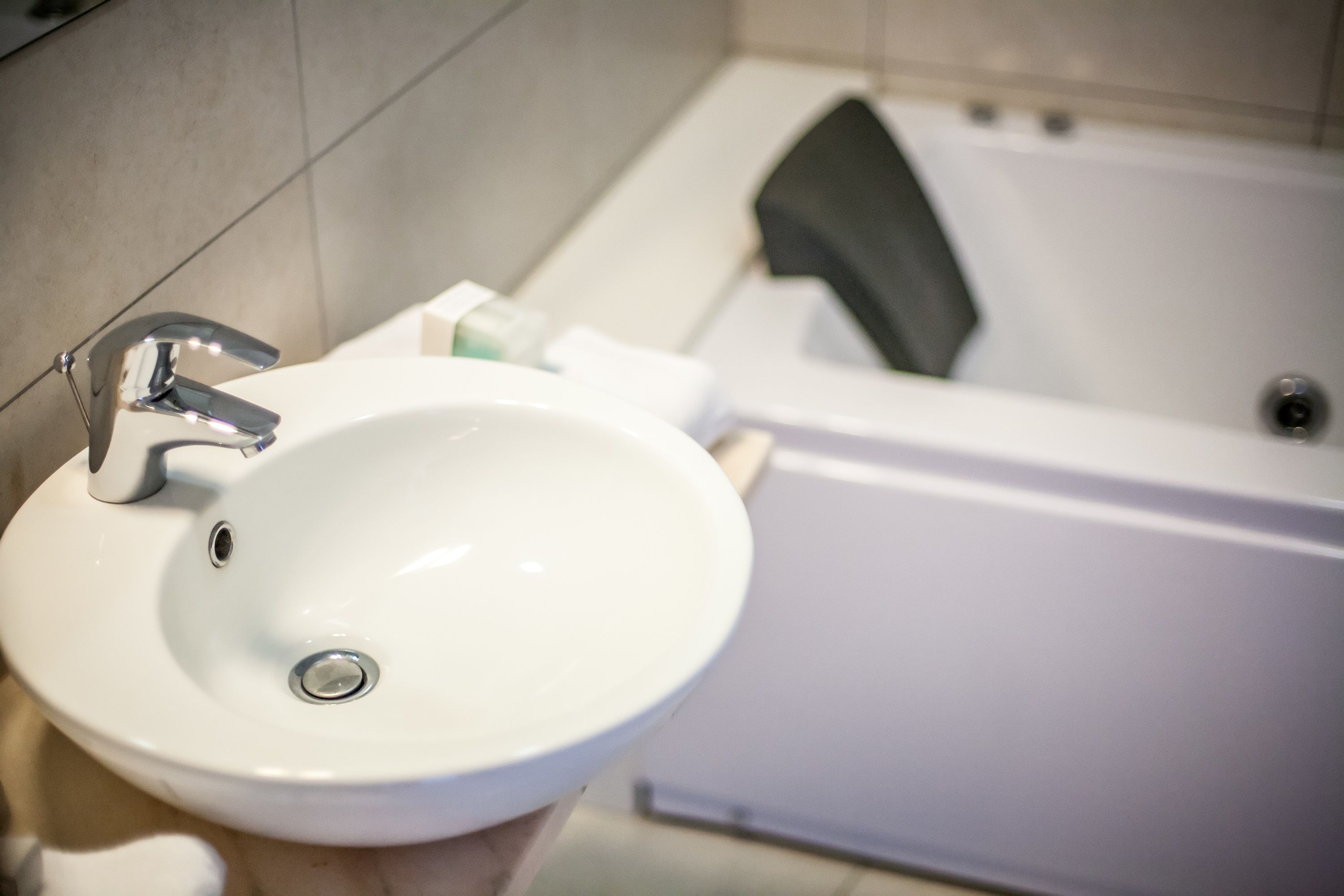 Un lavabo blanc dans la salle de bain, avec un robinet chromé, une baignoire et une serviette accrochée au mur.