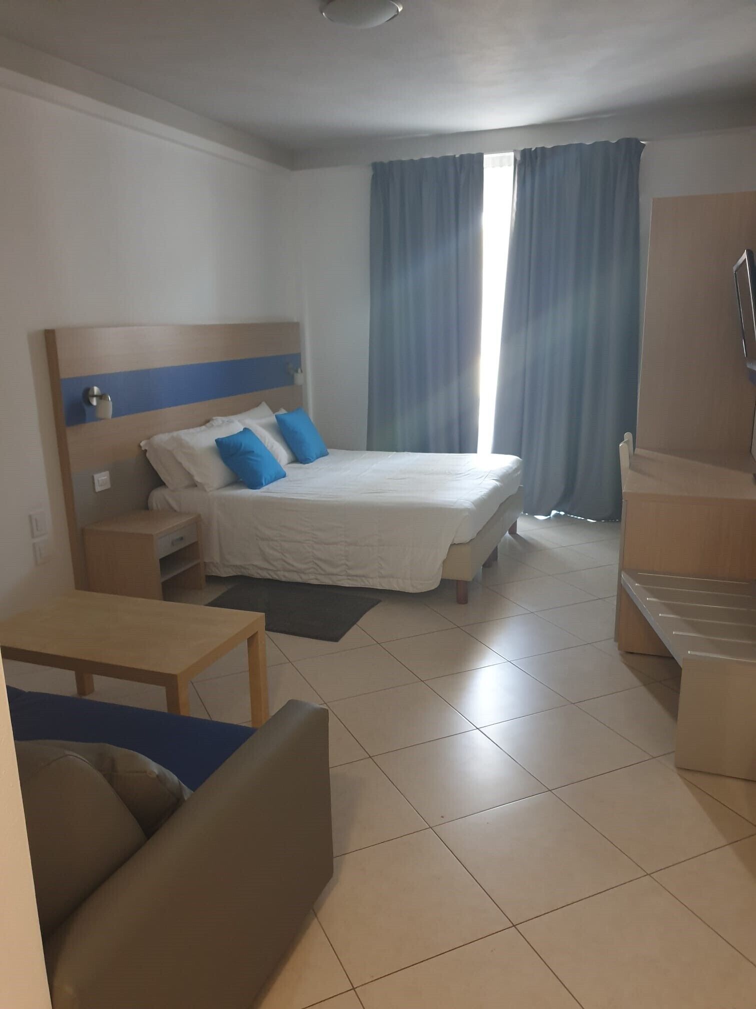 A hotel room with a bed, a desk, a chair, and a sofa.