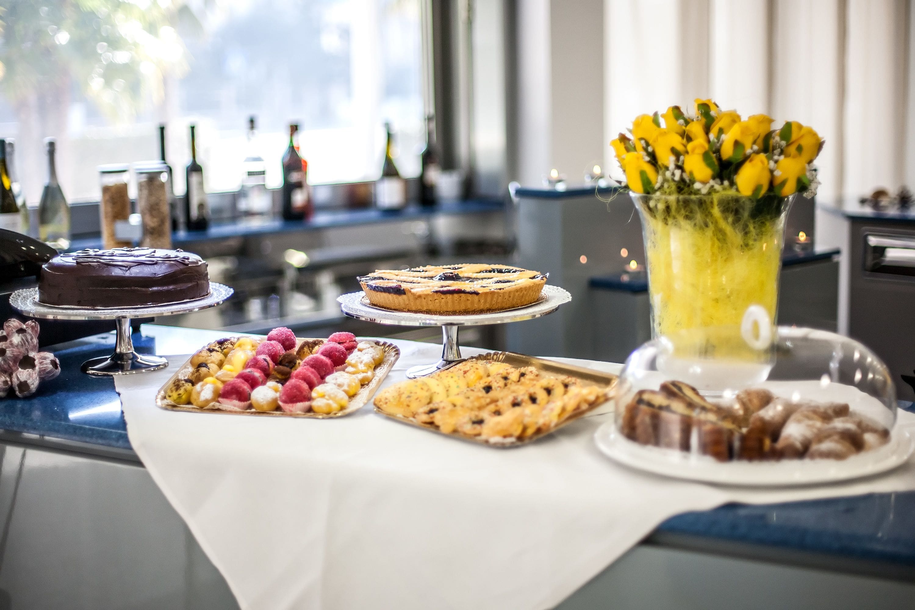 A dessert table with various cakes and pastries, a floral arrangement, and a bottle of champagne.