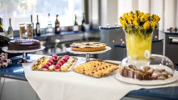 A dessert table with various cakes and pastries, a floral arrangement, and a bottle of champagne.