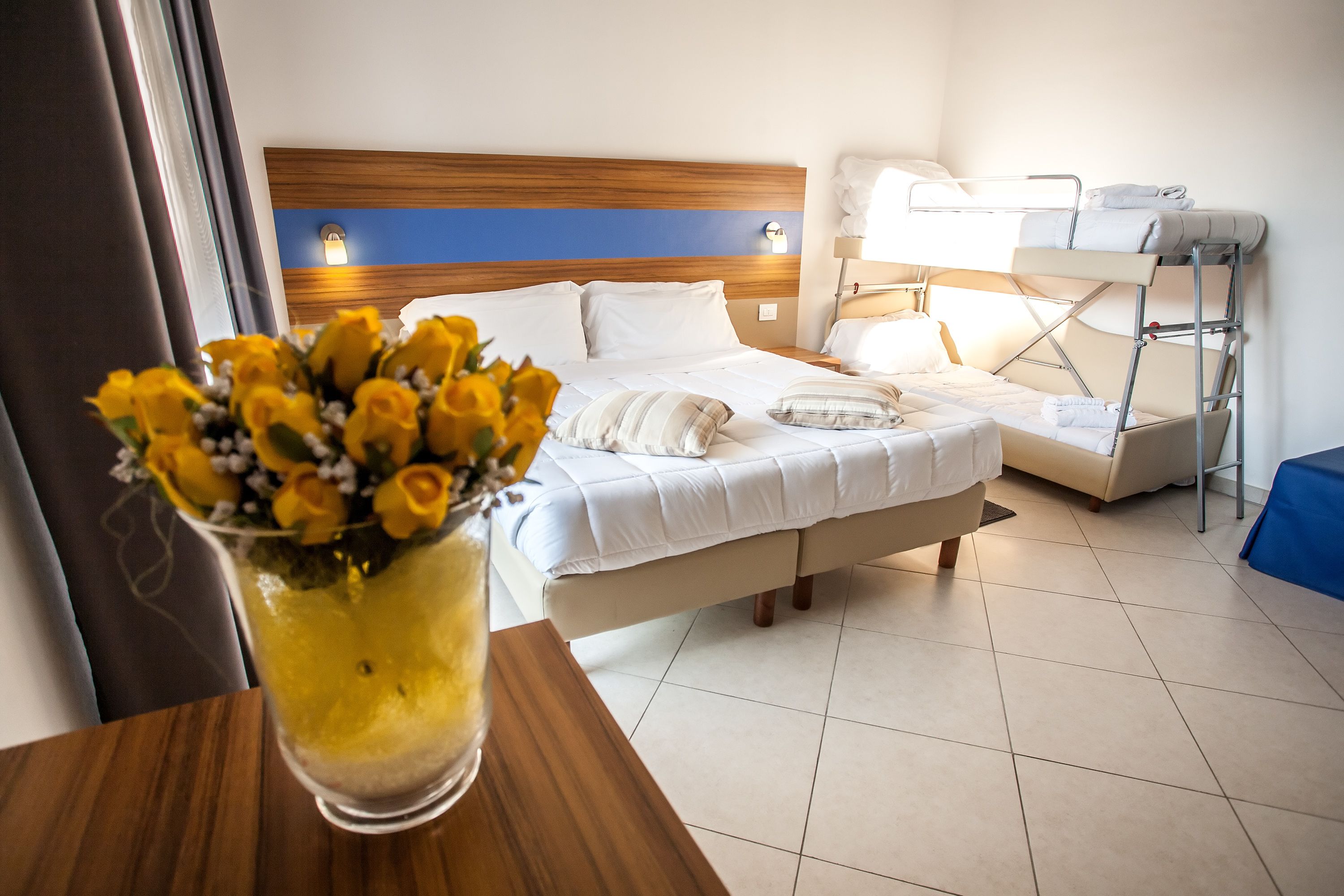 Una camera d'albergo con un letto, un comodino, una lampada e un letto a castello.