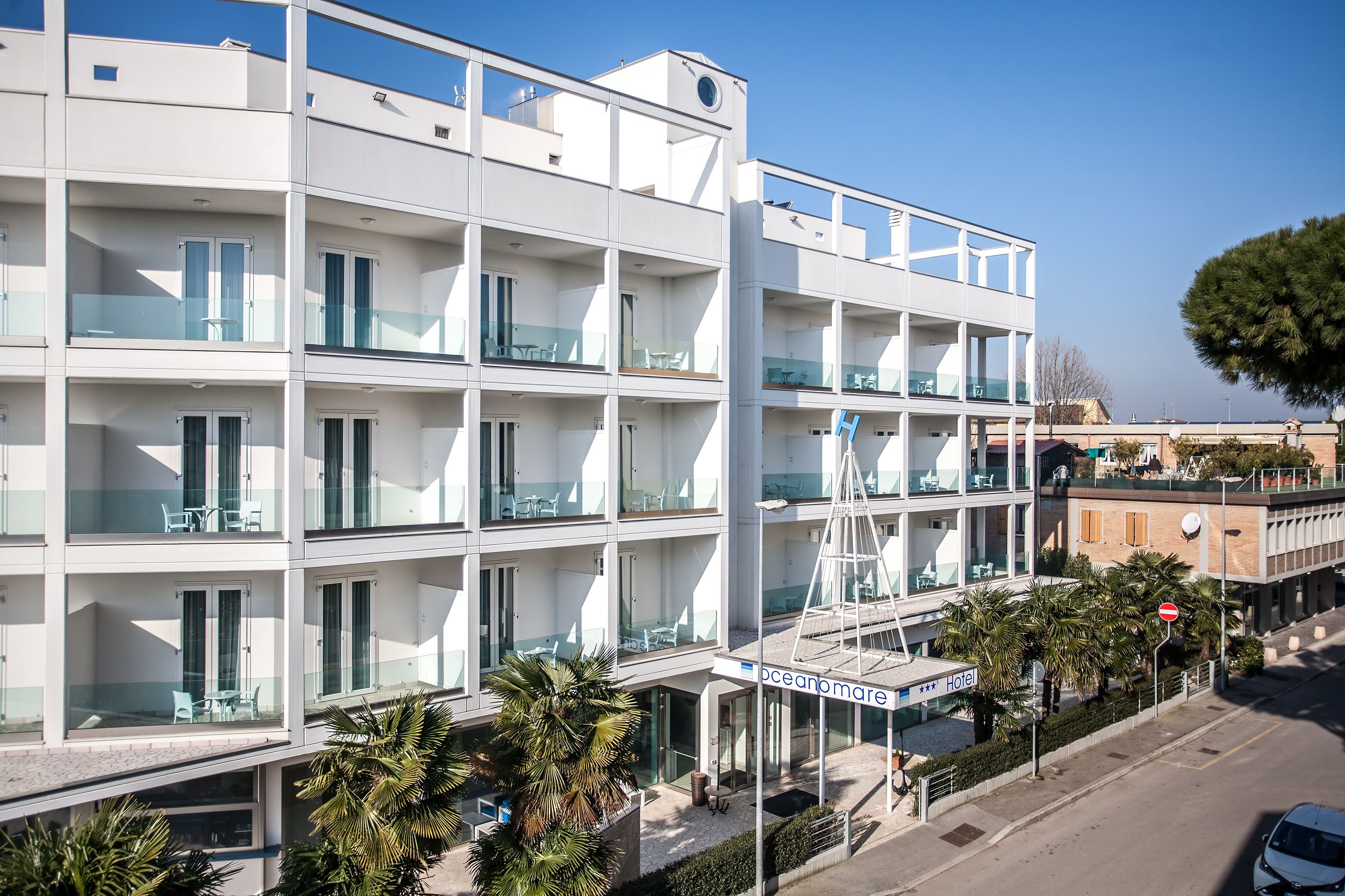 Un hotel de varios pisos con balcones, cielo despejado y palmeras.