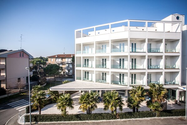 Un hôtel moderne à plusieurs étages, doté de balcons, d’un espace extérieur couvert et de palmiers.