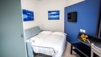 Un dormitorio con una cama, un escritorio con silla, un televisor y dos cuadros colgados en la pared.